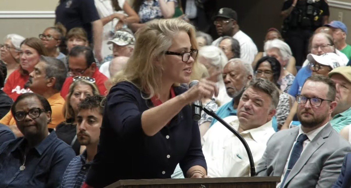 Heidi Pacella of Homer Glen delivering public comment at the microphone before the Illinois Commerce Commission forum on the Illinois American Water rate increase, in front of a packed room at the Bolingbrook Community Center, July 14, 2026.