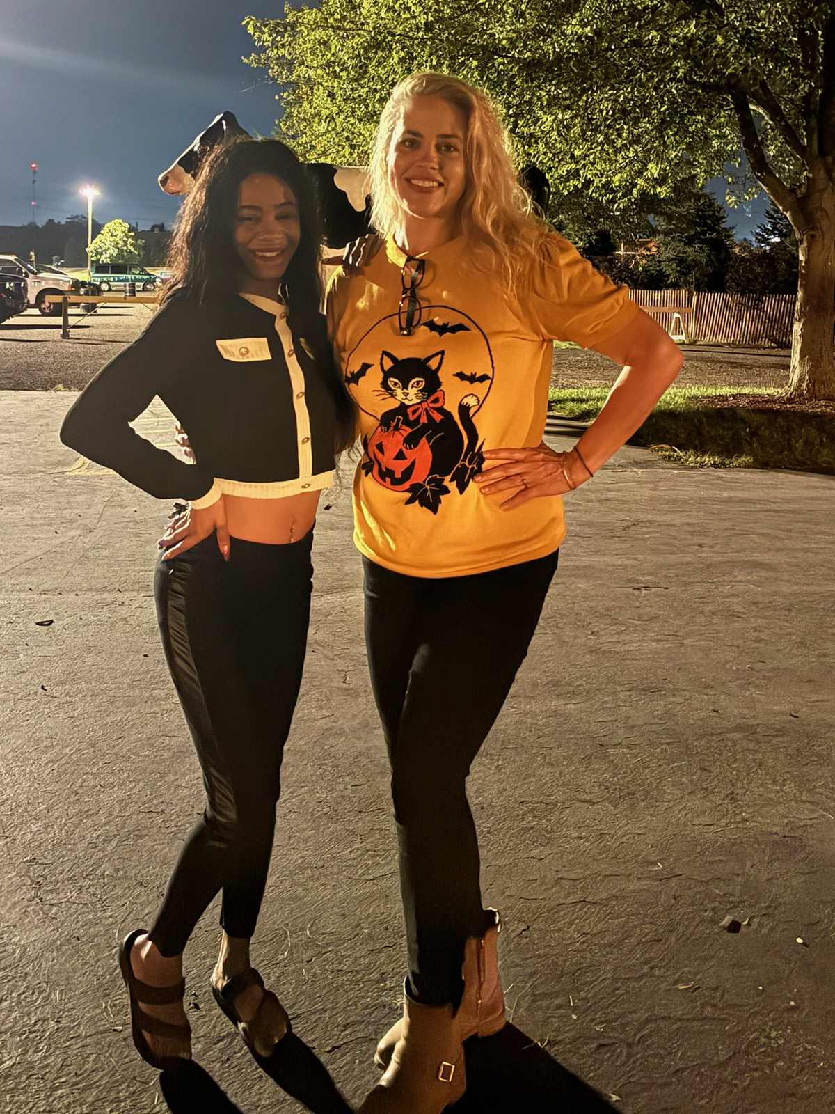 Heidi, in a yellow t-shirt, arm in arm with a guest in front of Bengtson's cow statue at night.