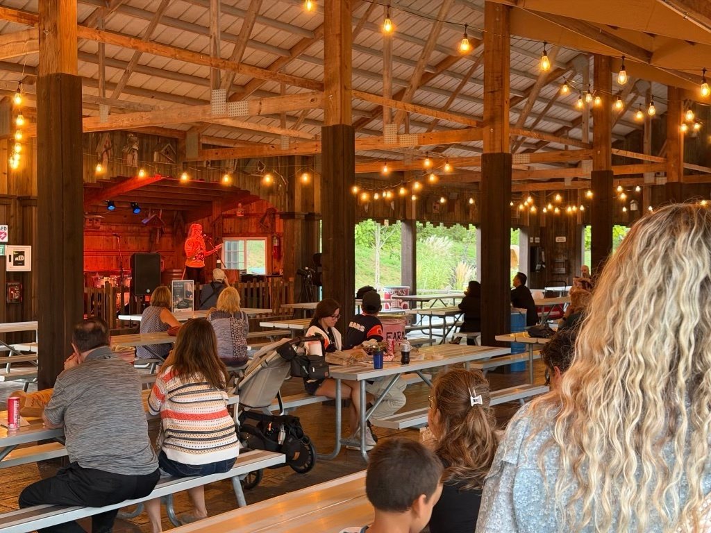 Families at picnic tables under the pavilion's string lights, with Heidi on the stage in the distance.